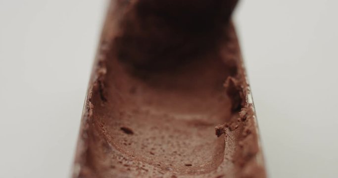 Taking a thin layer of artisanal chocolate ice cream from a small narrow stainless steel pan with a spoon