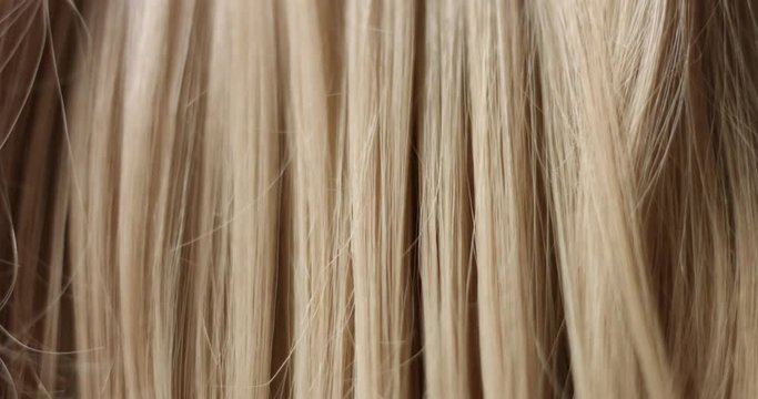 Close up video of combing long wavy woman's blond hair with a black hair comb