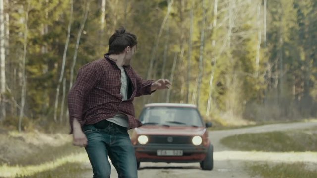 Scared man running in slow motion from the chasing car through the forest road