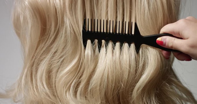 Close up video of combing long wavy woman's blond hair with a black hair comb