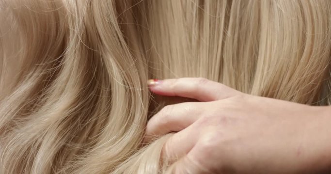 A woman's hand with bright manicure running through long wavy blond hair