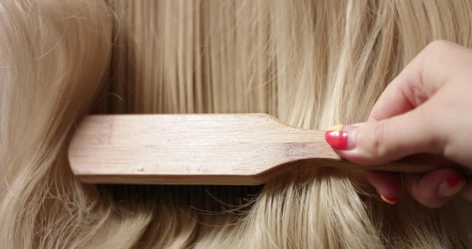 Close up shot of brushing long wavy woman's blond hair with a hairbrush
