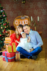 Fototapeta na wymiar happy family sitting on the floor near boxes with gifts and smiling, in the background festive Christmas tree