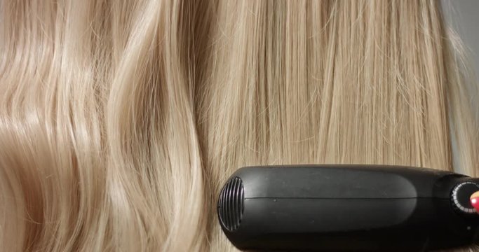 Using a black hair straightener to style long blond wavy woman's hair, close up video