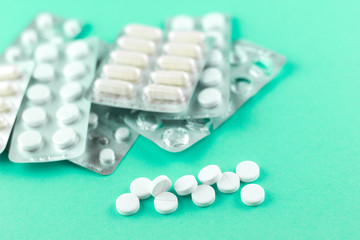 Full and empty packs of white capsules and pills packed in blisters with copy space on aquamarine background. Focus on foreground, soft bokeh