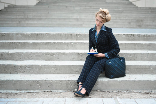 Young business woman in business suit sitting on the on stairs with the notepad
