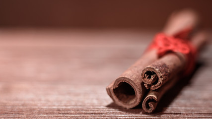 Horizontal shot of cinnamon sticks tied with red ribbon closeup on wooden background blur.