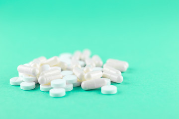 Obraz na płótnie Canvas Close up white pills and capsules on aquamarine background with copy space. Focus on foreground, soft bokeh. Pharmacy drugstore concept
