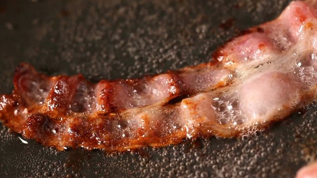 Close up of bacon slice frying on pan in sunflower oil