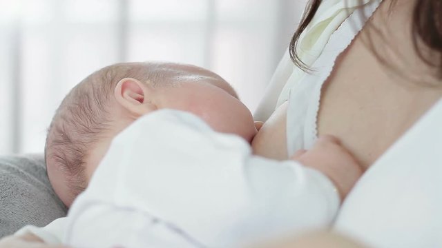 Young mother feeding breast her baby at home in bright room