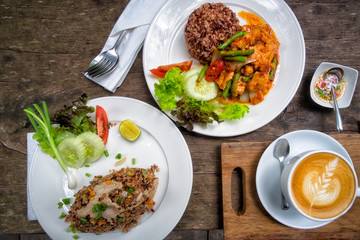 Fried chilly paste with pork, meat with stream rice, Fried rice and hot latte coffee on wooden table.