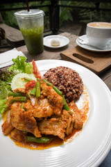 Fried chilly paste with pork, meat with stream rice and ice tea on wooden table.