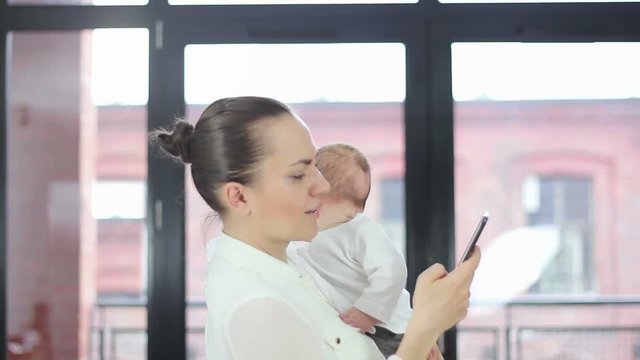 Working mother holding baby and checking mobile phone