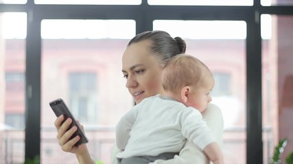 Working mother holding baby and checking mobile phone