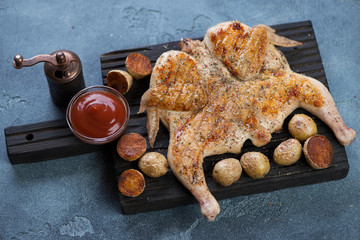 Fototapeta premium Black wooden serving board with roasted tapaka chicken, cherry potatoes and sauce, studio shot