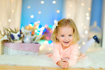 happy little girl lying on the floor against the backdrop of festive garlands and laughing cheerfully.