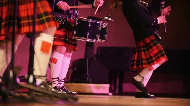 Traditional scottish band musicians in white socks and kilts singing with bagpipes on the stage