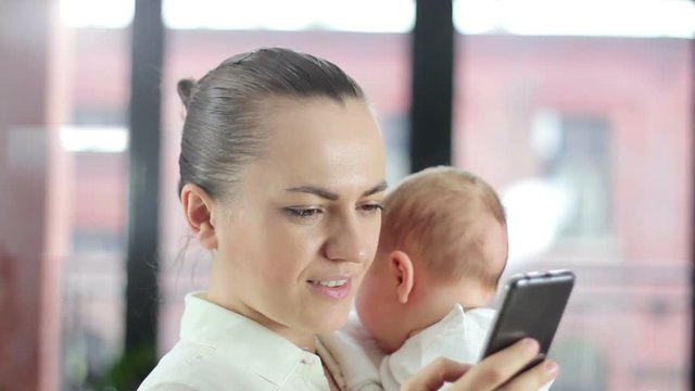 Working mother holding baby and checking mobile phone