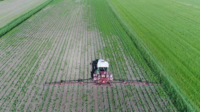 Aerial bird view footage flying behind tractor spraying chemicals over young corn field mostly glyphosate is used as pre-harvest herbicide and harvest aid on crops and is used to kill weeds 4k quality