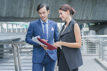 Professional businesswoman holding document while standing outside discuss new project with businessman in cityscape background
