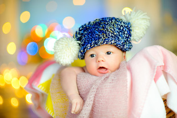 beautiful newborn baby lies in a basket on a soft blanket, in the background festive lights.