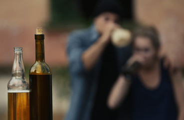 Bottles with alcohol on blurred view of drunk people
