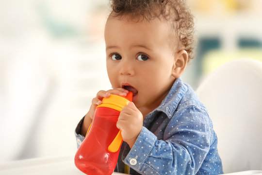 Cute little baby with bottle of water sitting on chair in room