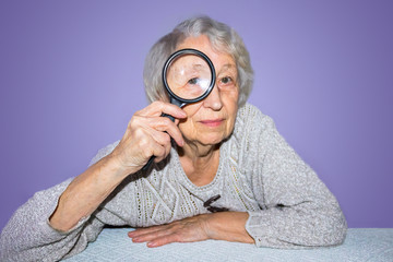 portrait of senior woman looking through a magnifying glass over lilac background