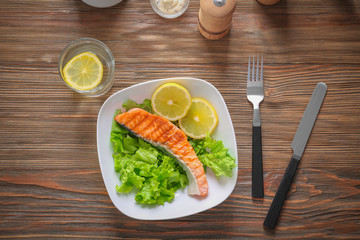Plate with tasty grilled salmon and lemon slices on table