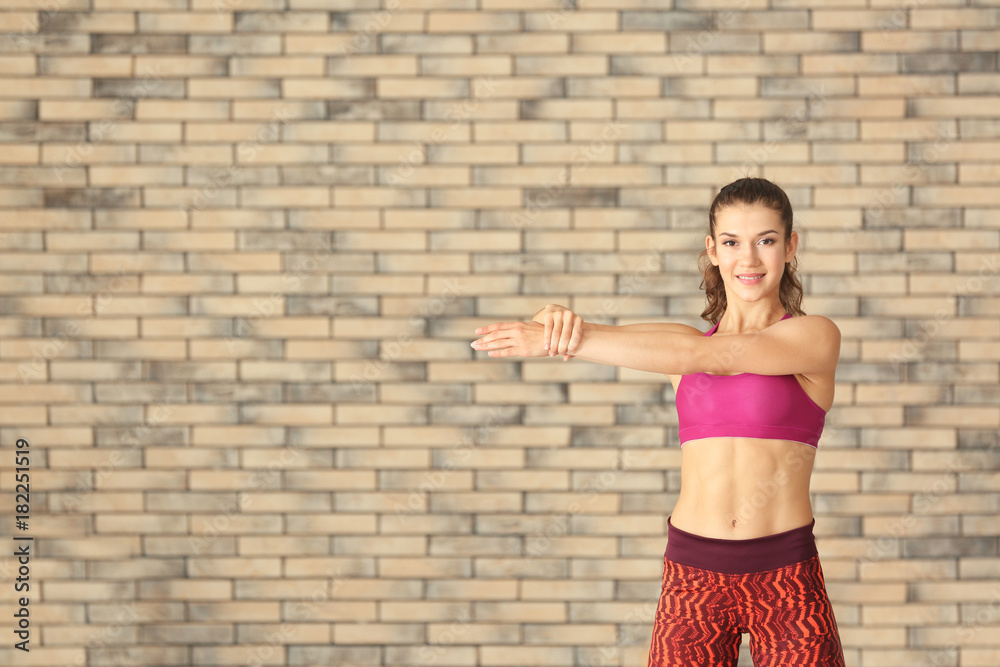 Wall mural Sporty young woman training against brick wall