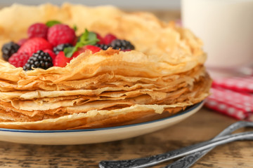 Plate of delicious thin pancakes with berries on wooden table, closeup