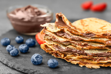 Delicious thin pancakes with chocolate paste and berries on slate plate, closeup