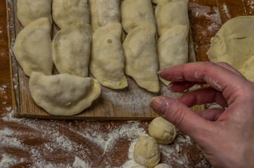 The hands of a woman cook cooked on a table of flour dough and make vareniki