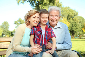 Elderly couple with grandson sitting on bench in park