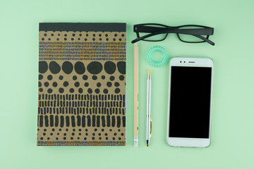 Creative flat lay photo of workspace desk with eyeglasses, pen, pencil and notebook, minimal style on green background. Minimal concept 