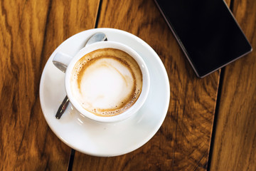     A cup of coffee and smart phone on a woden table in cafe, soft warm filter, lens flare 