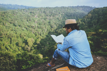 Asian man travel relax in the holiday. seats relax read books on rocky cliffs. On the Moutain. In Thailand