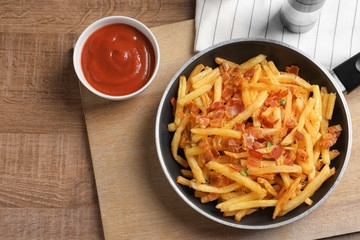 Frying pan with french fries and bacon on table