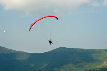 Tandem flies over a mountain valley on a sunny summer day. Paragliding in the Carpathians in the summer. Passenger on the paraglider holds a selfie stick and shoots the video.