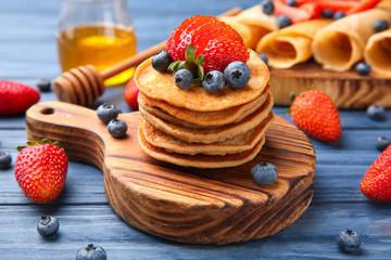 Board with buckwheat pancakes and berries on wooden table