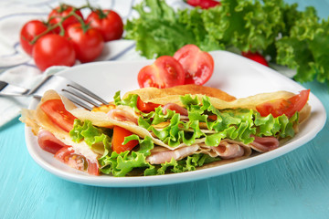 Plate with thin buckwheat pancakes, bacon and vegetables on table