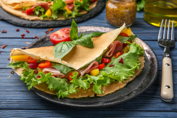 Plate with thin buckwheat pancake, bacon and vegetables on table