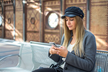 Young woman using phone while waiting for train at railway station.