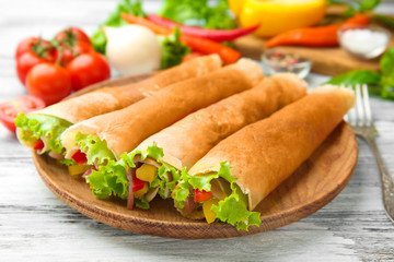 Plate with rolled buckwheat pancakes, bacon and vegetables on table