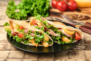 Plate with thin buckwheat pancakes, bacon and vegetables on table