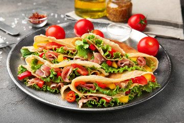 Metal dish with thin buckwheat pancakes, bacon and vegetables on table