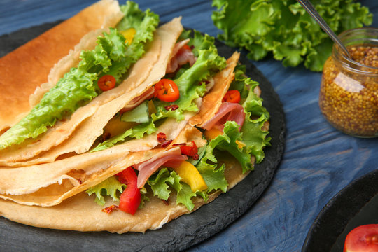 Slate plate with thin buckwheat pancakes, bacon and vegetables on table