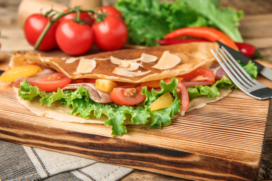 Board with thin buckwheat pancake, bacon and vegetables on table