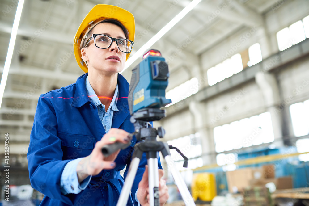 Wall mural serious concentrated female engineer focusing on survey line while making measurements at constructi