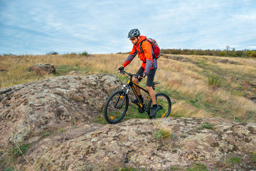 Fototapeta na wymiar Cyclist in Red Riding the Bike on Autumn Rocky Trail. Extreme Sport and Enduro Biking Concept.